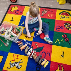 A child sits on a colorful play mat with toy animals lined up in a single row.