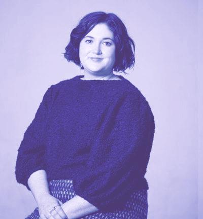 一张照片上，一个黑头发、穿着毛绒绒毛衣的女人坐在白色背景前