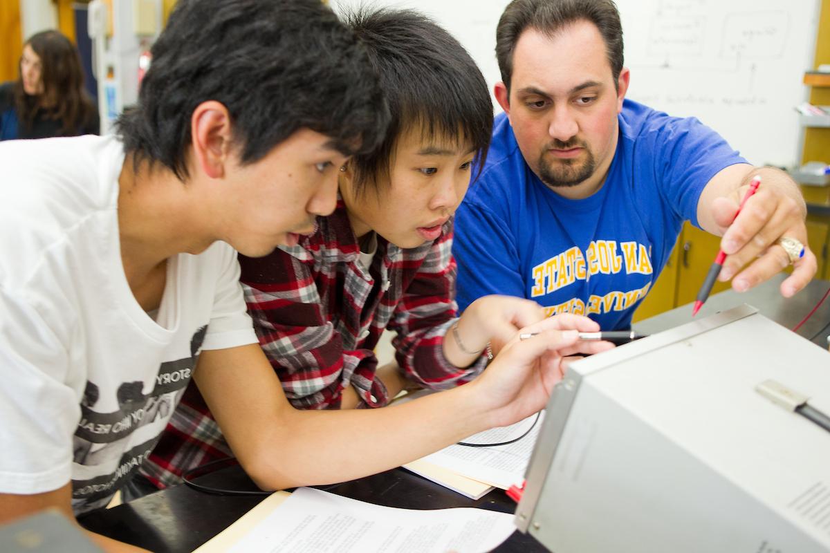 三个学生聚集在一个显示器周围，用铅笔指着它.